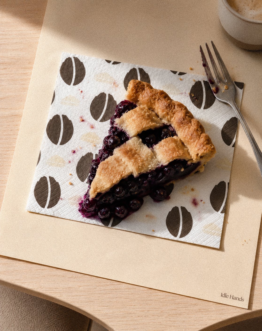 Idle Hands patterned napkin on a café table with a mug and an espresso