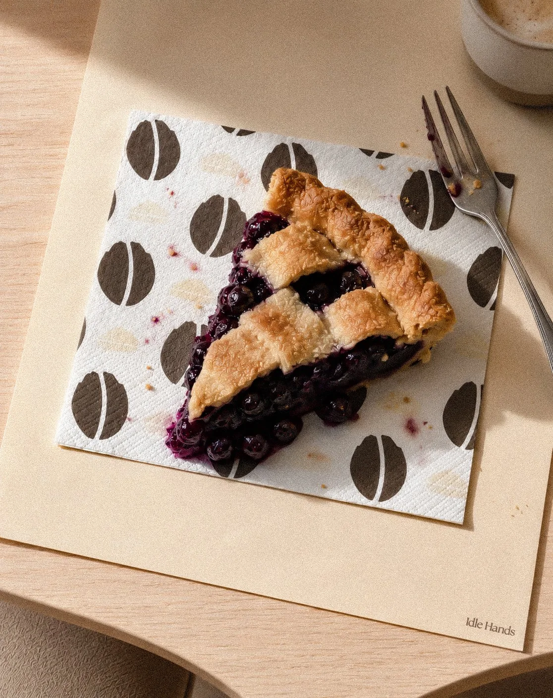 Idle Hands patterned napkin on a café table with a mug and an espresso