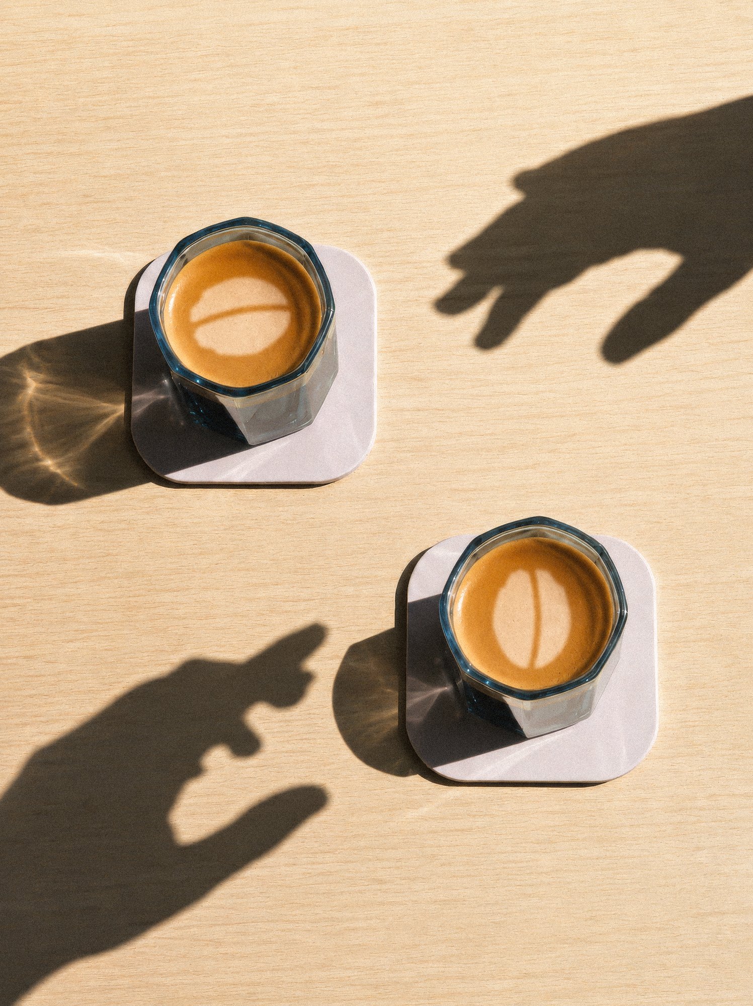 Two Idle Hands espressos with the bean mark in the crema, hand shadows reaching in