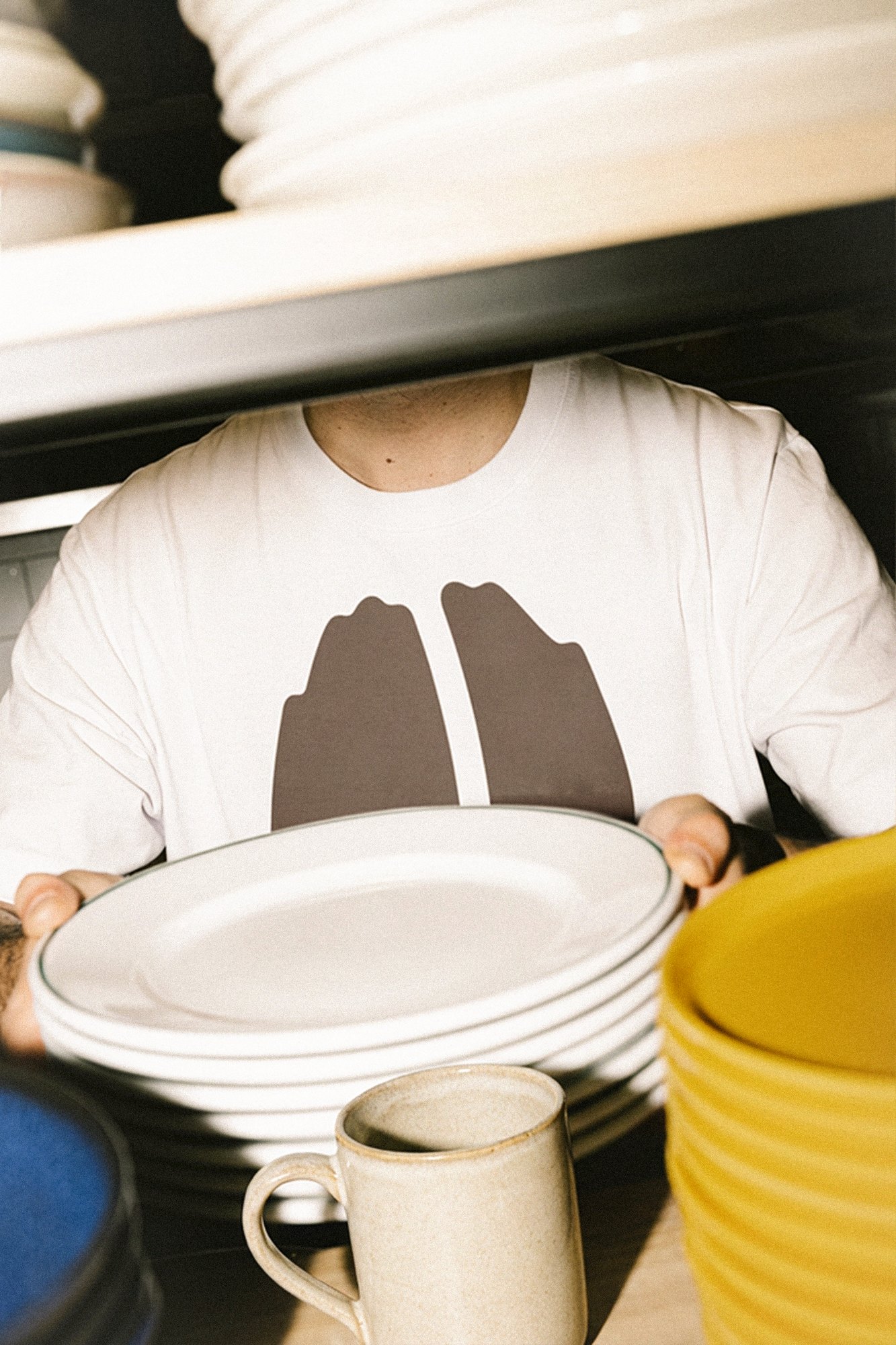 The Idle Hands tee, the bean mark across the chest, worn behind a stack of plates