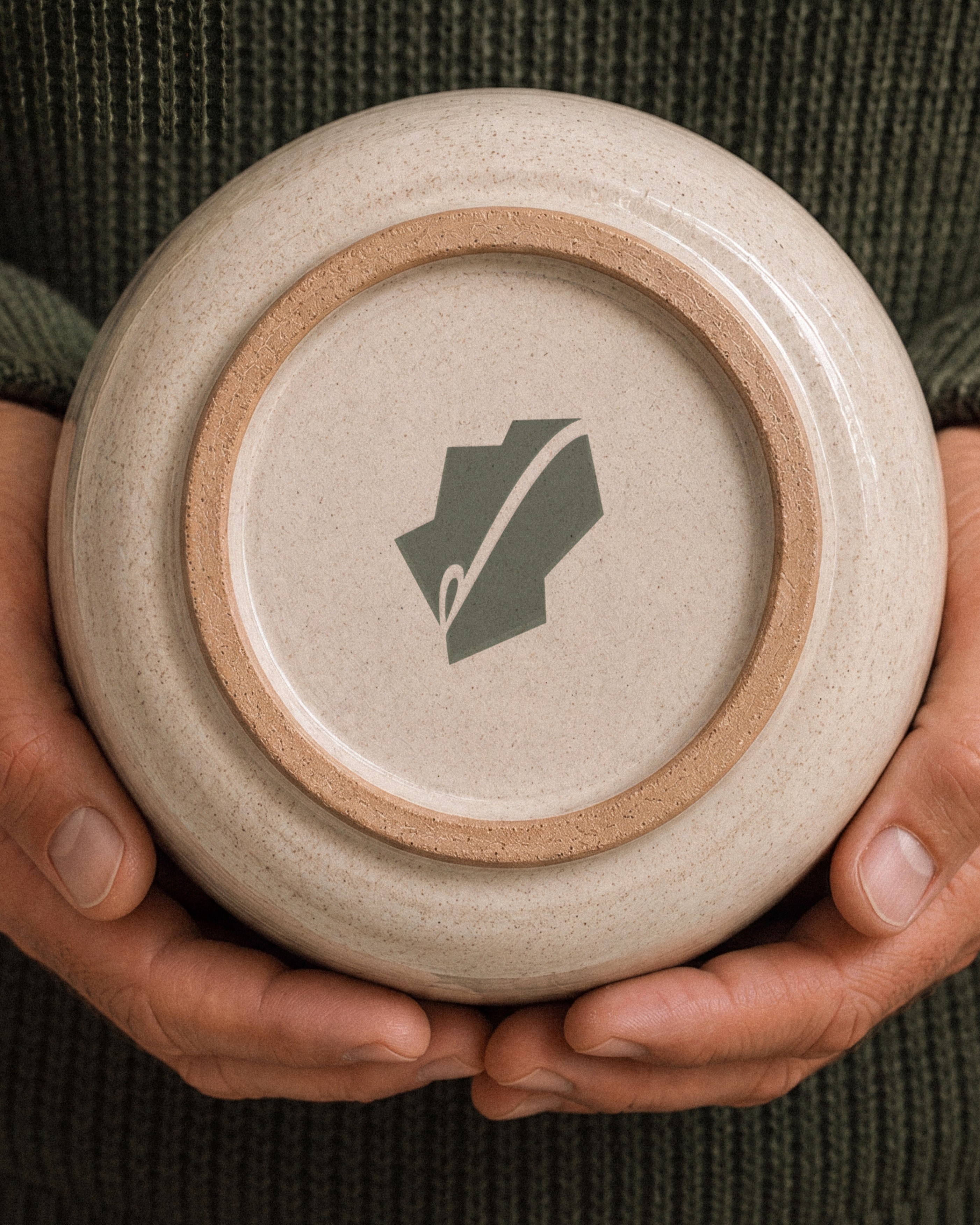 The Patch mark stamped on the base of a stoneware pot, held in two hands