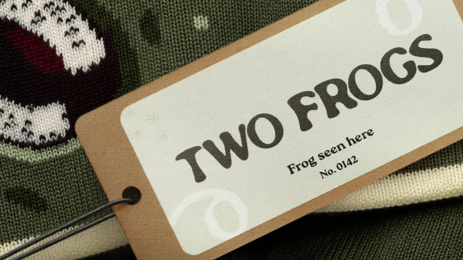 Two Frogs kraft hang tag reading Frog seen here, No. 0142, on a green knit