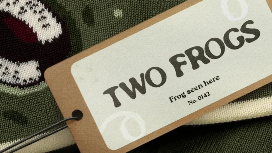 Two Frogs kraft hang tag reading Frog seen here, No. 0142, on a green knit